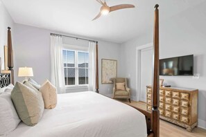 A bedroom with a four-poster bed, a ceiling fan, a window with blinds, a chair, a TV, and a wooden dresser. - Redfish Village M1-309 (Santa Rosa Beach)