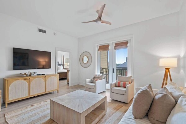A modern living room with a flat-screen TV, a wooden cabinet, a round mirror, and a ceiling fan. - Redfish Village M1-309 (Santa Rosa Beach)
