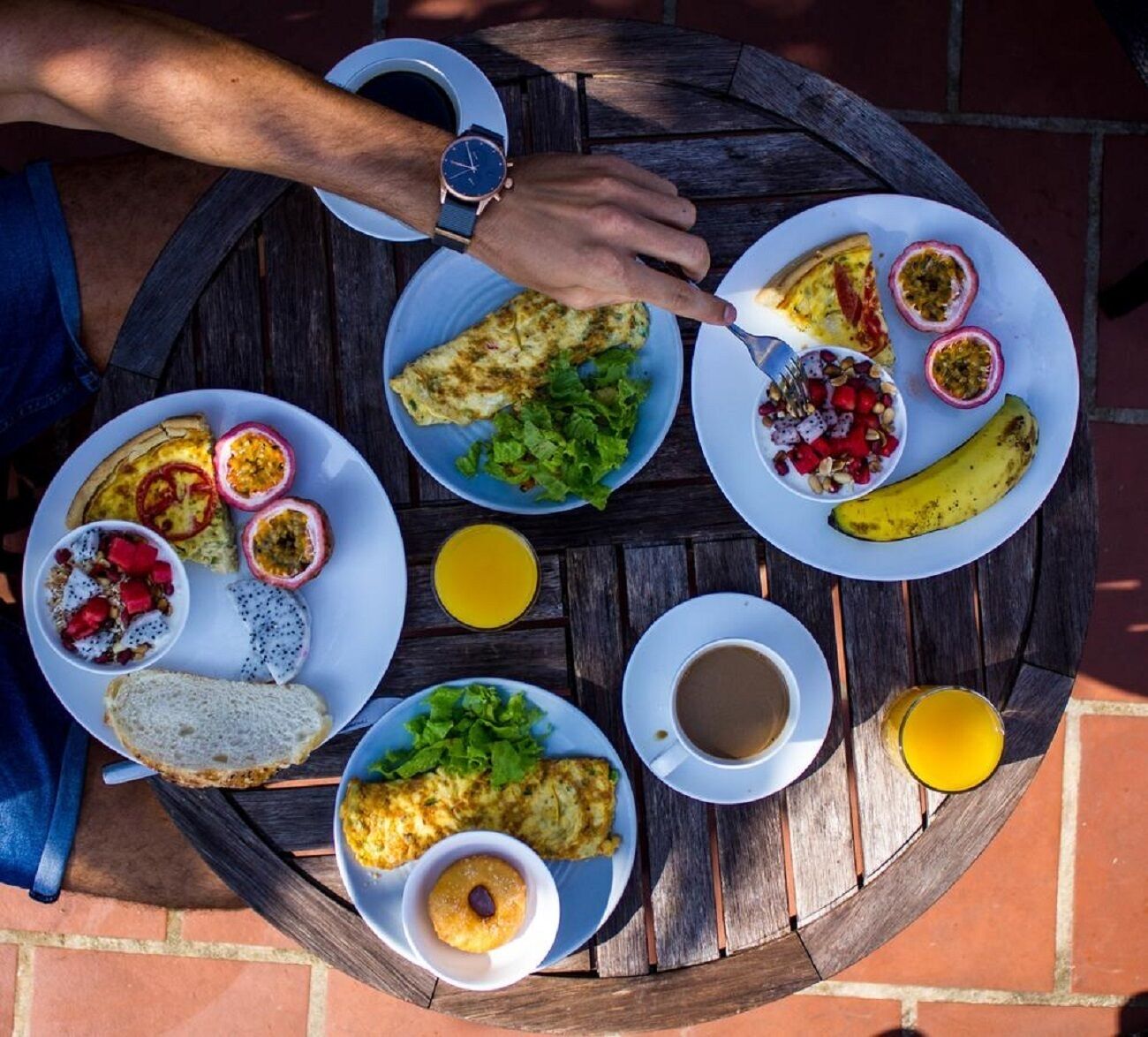 Une table ronde en bois, sur laquelle sont disposés divers aliments pour le petit-déjeuner, notamment des tartines, des fruits et une tasse de café.