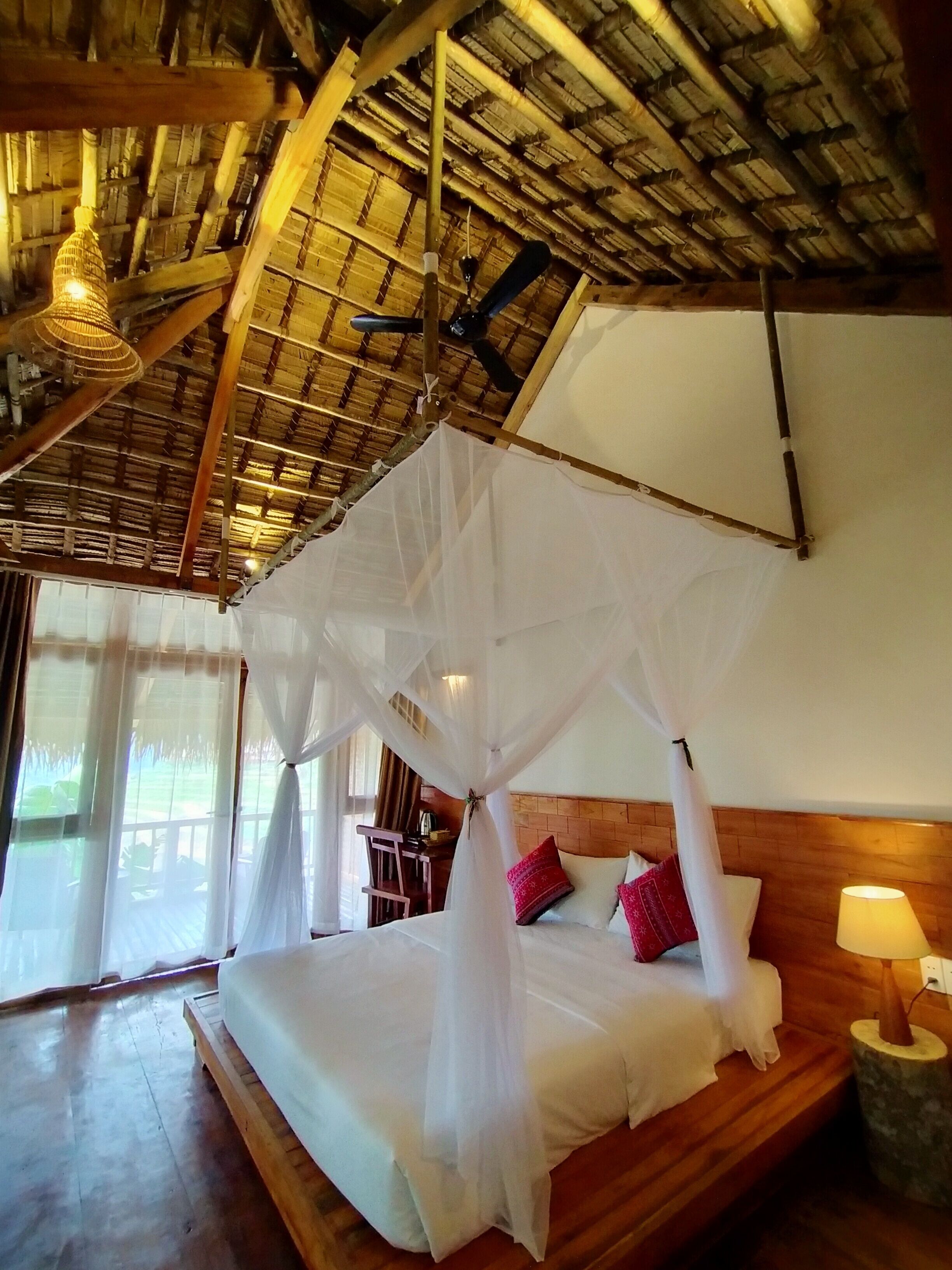 Una habitación con cama bajo un dosel, vigas de madera en el techo y una ventana con cortinas.
