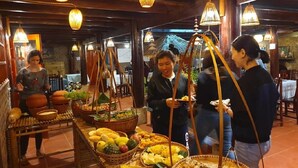 A restaurant interior with wooden beams, hanging lanterns, and a buffet table with various fruits and vegetables.