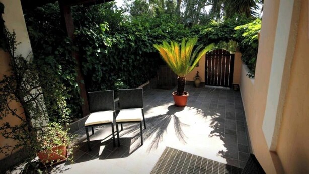 En overdækket terrasse med to stole, en potteplante og en låge.