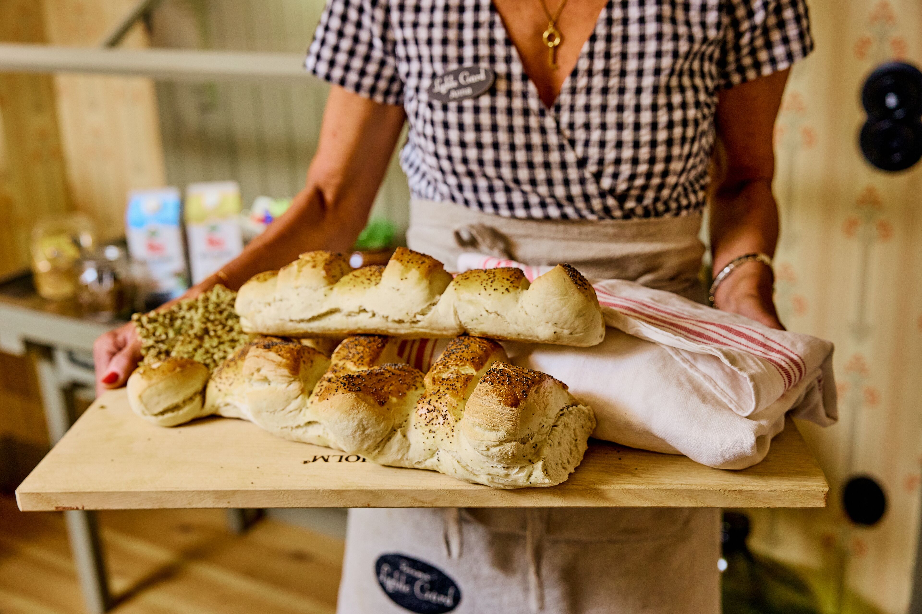 A person holding a tray with bread rolls and a cloth.