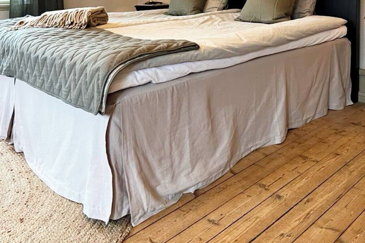 A bedroom with a large bed, a wooden floor, a lamp, and a wall-mounted light fixture.
