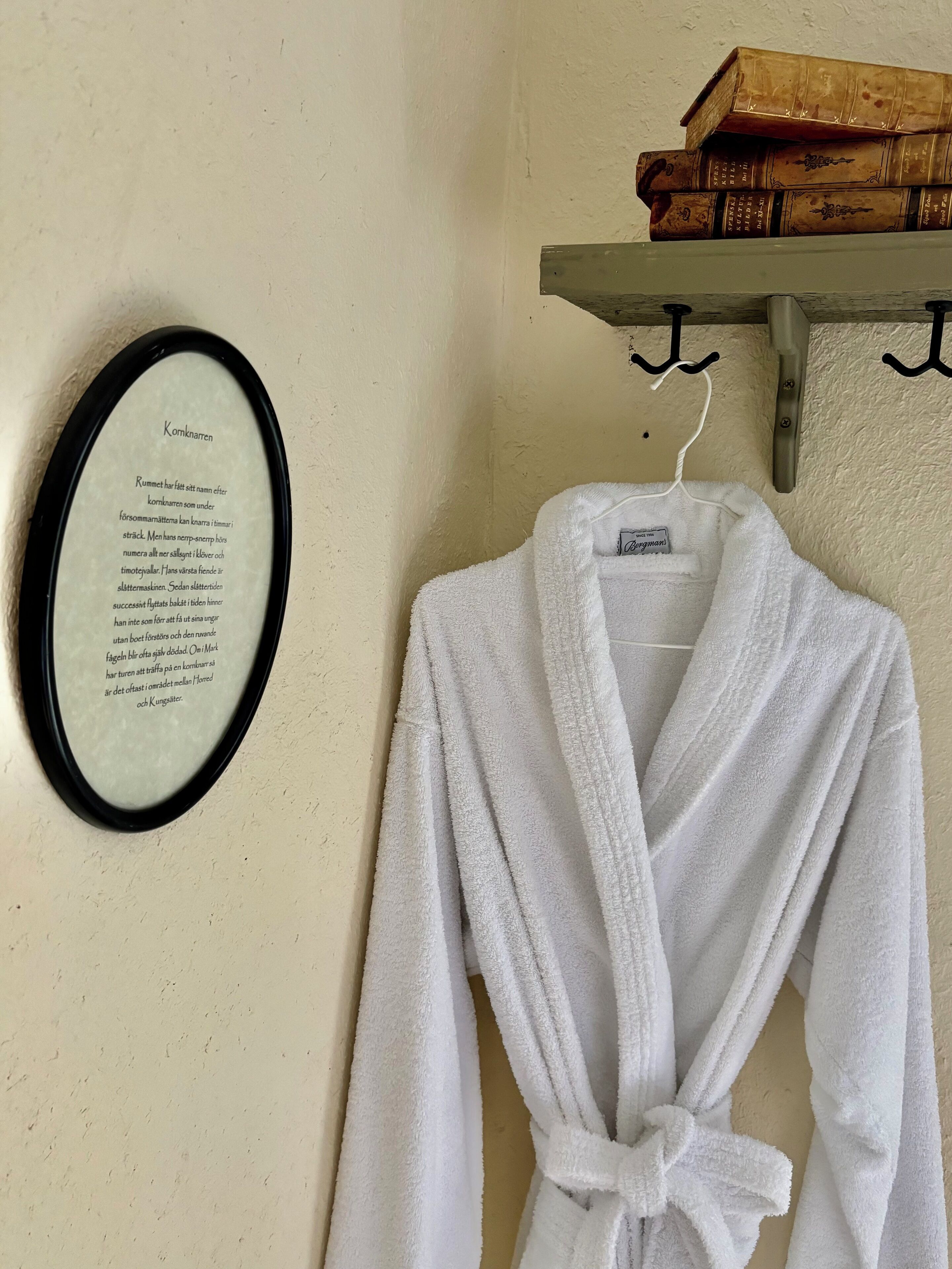 Un poème encadré accroché au mur, un peignoir blanc suspendu à un crochet et une pile de livres sur une étagère.