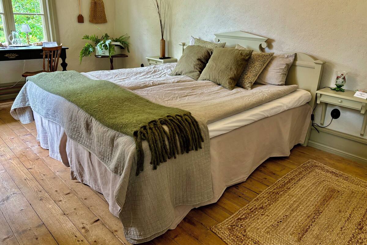 A double bed with a green throw blanket, a bedside table with a lamp, and a nightstand with a phone.