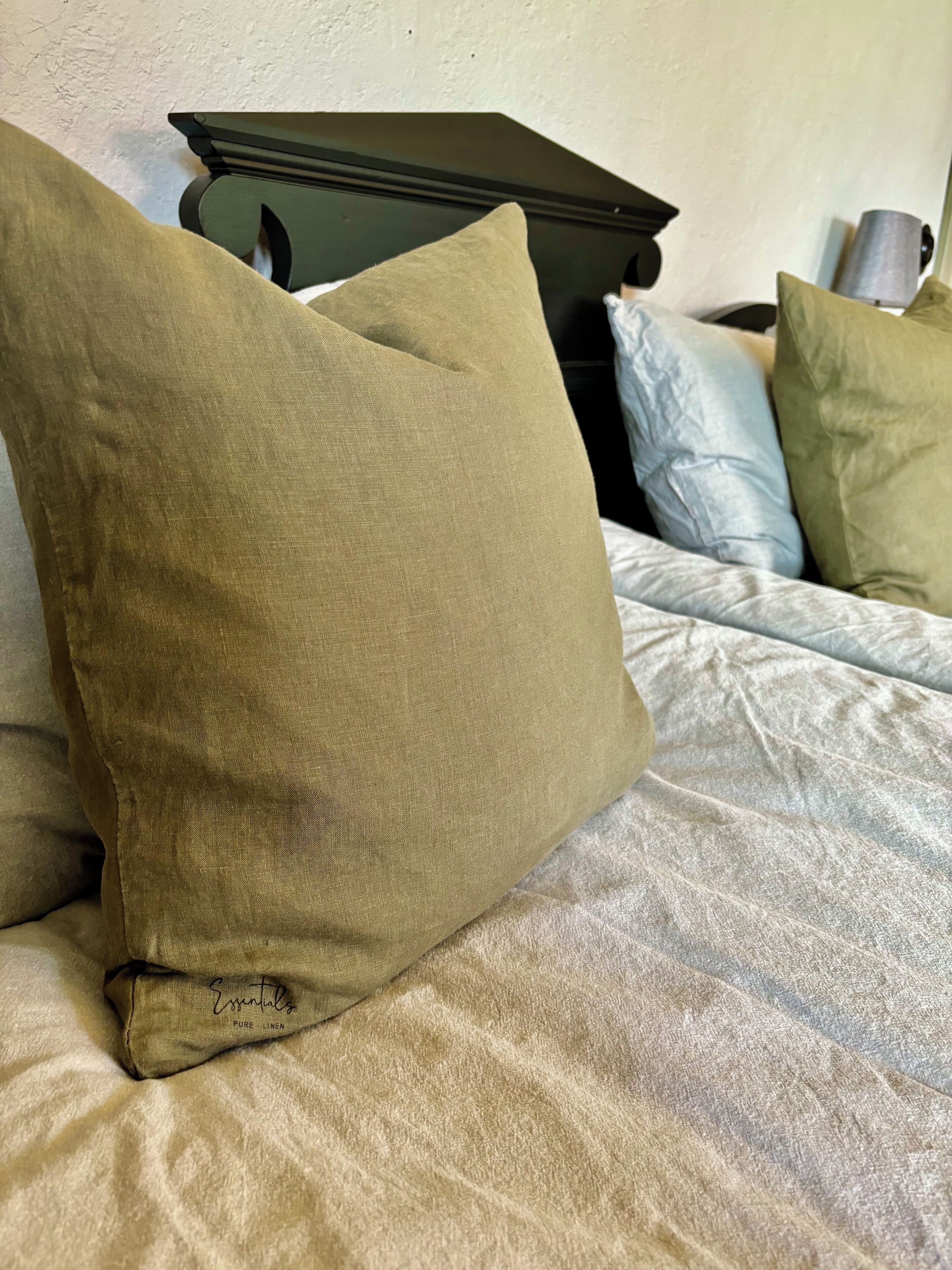A bed with beige bedding and a single brown pillow.
