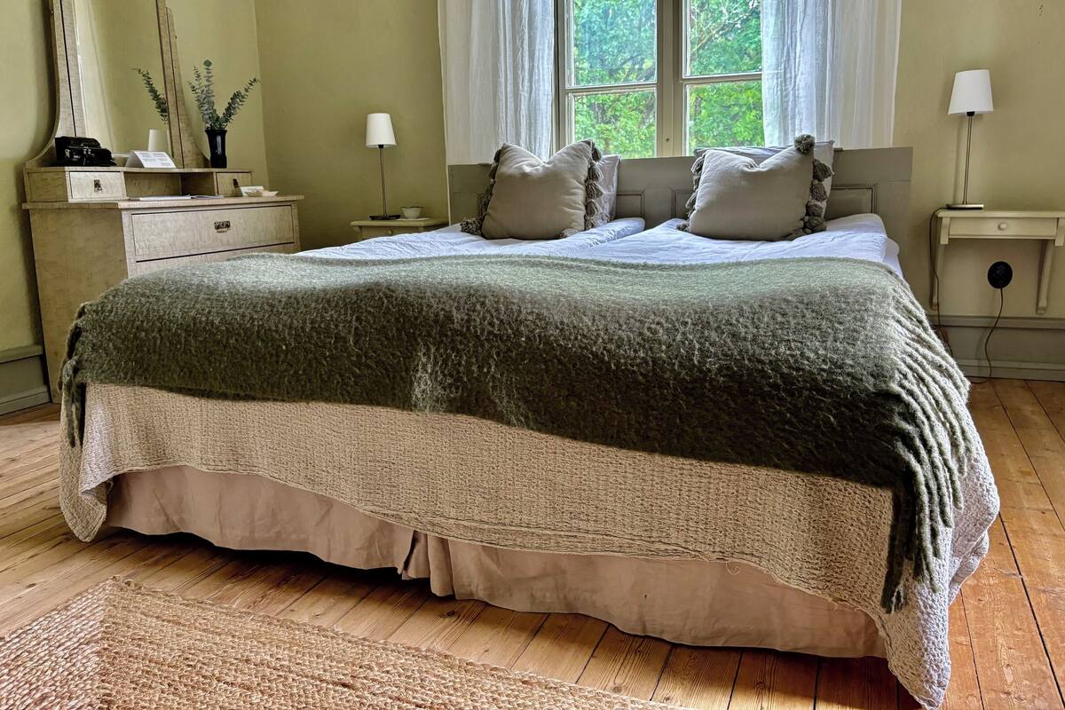 A bedroom with a large bed, a nightstand, a dresser, a mirror, and a window with curtains.