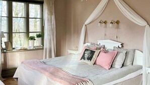 Een slaapkamer met een hemelbed, een houten vloer en een raam met gordijnen.