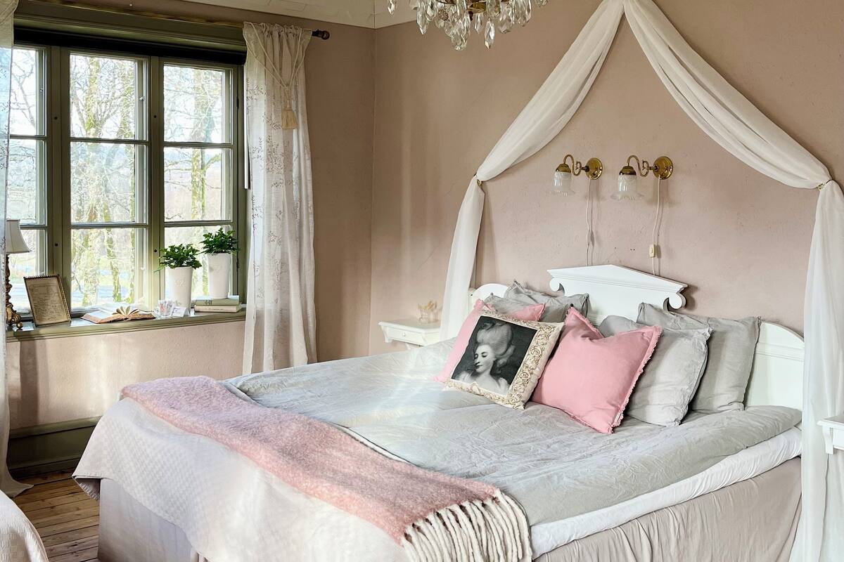 A bedroom with a canopy bed, a wooden floor, and a window with curtains.