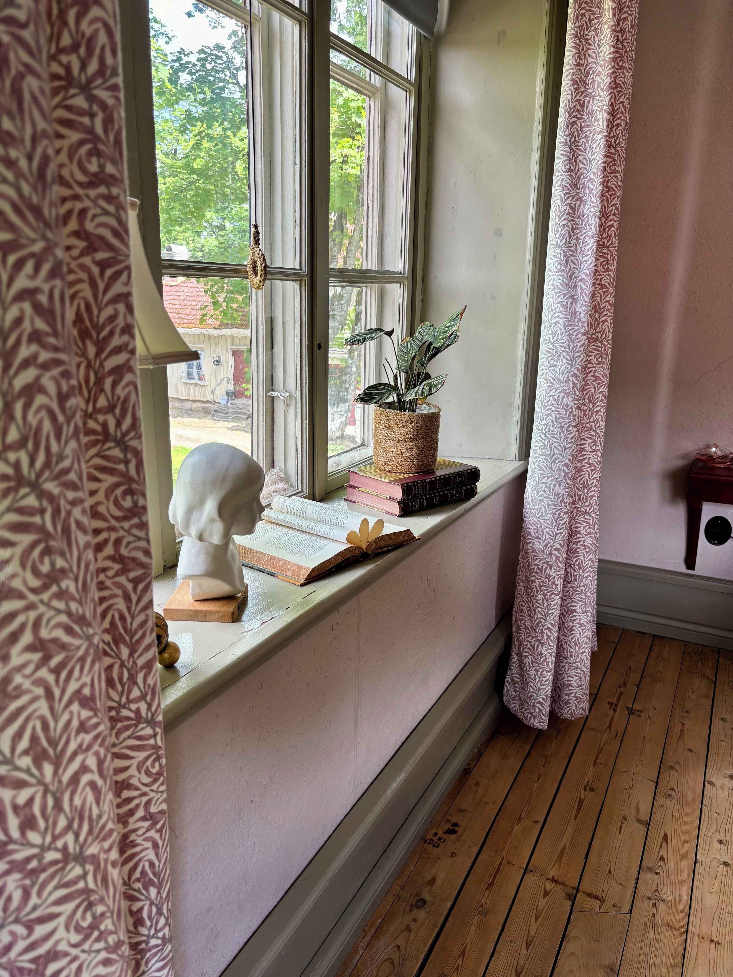 Um quarto com parapeito de janela decorado com livros, um busto e um vaso de planta.