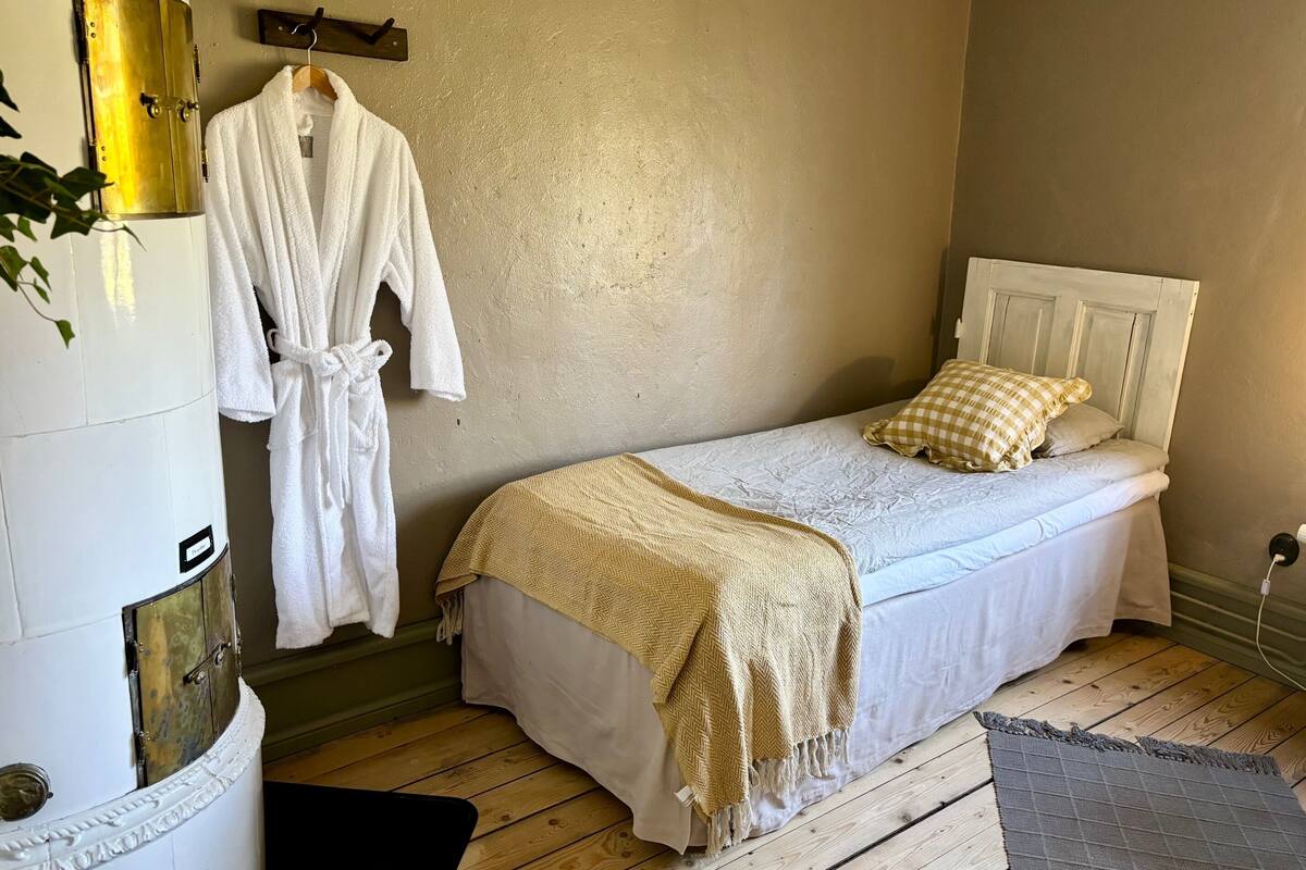 A bedroom with a bed, a white robe hanging, and a wooden floor.