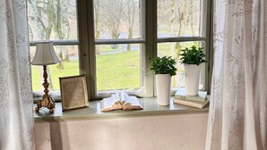 Een kamer met een groot raam, een lamp, een ingelijst document en twee potplanten op de vensterbank.