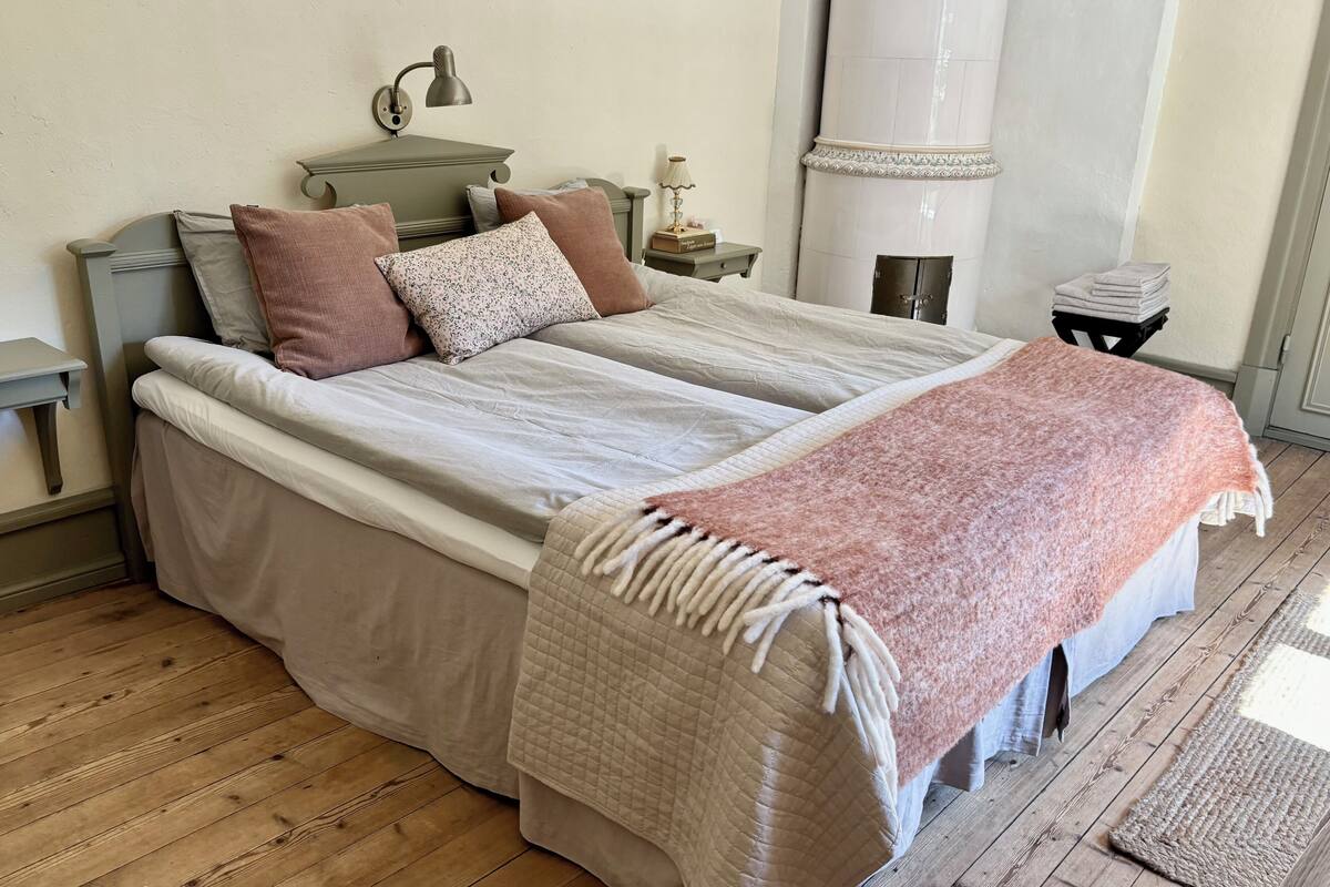 A double bed with a quilted cover, two bedside tables with lamps, a nightstand, and a small cabinet.