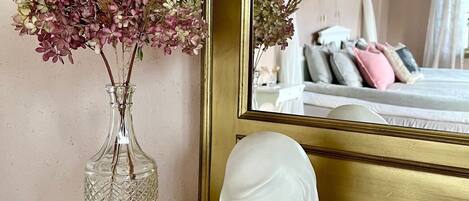Ett rum med en säng, en spegel, en vas med torkade blommor, en byst och en liten prydnadstallrik.
