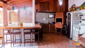 A rustic kitchen with wooden beams, a tiled backsplash, and a central island with bar stools. - Hostel House Santinho (Florianópolis)