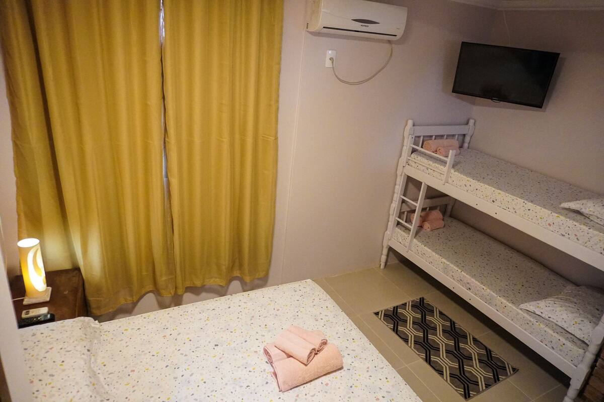Ein Zimmer mit einem Bett, einem an der Wand befestigten Fernseher und einem Fenster mit Vorhängen.