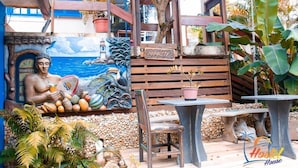 A mural with a tropical scene, a wooden bench, a table, and a chair in a garden area. - Hostel House Santinho (Florianópolis)