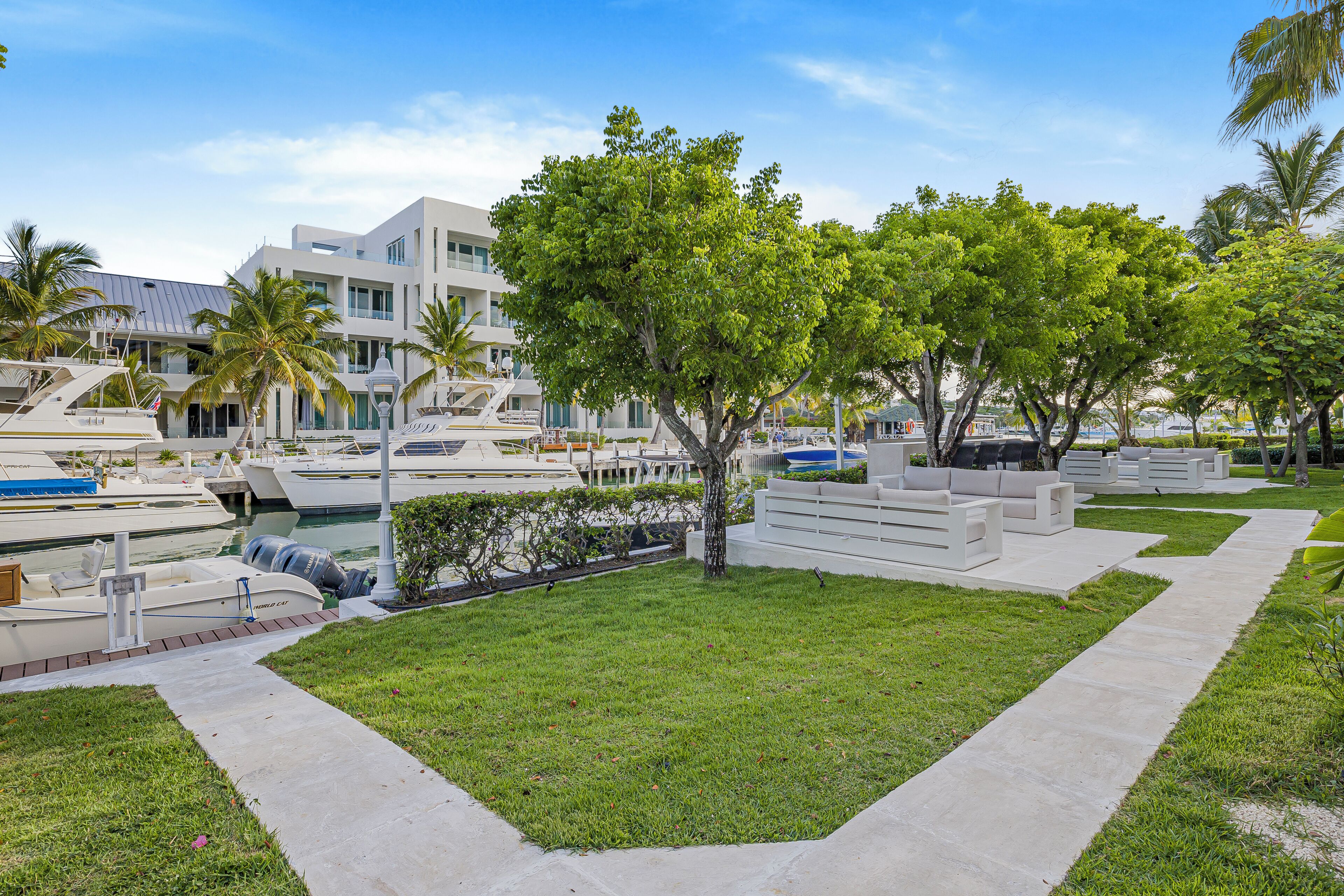 A marina with boats docked, a grassy area with benches, and a modern building with large windows.