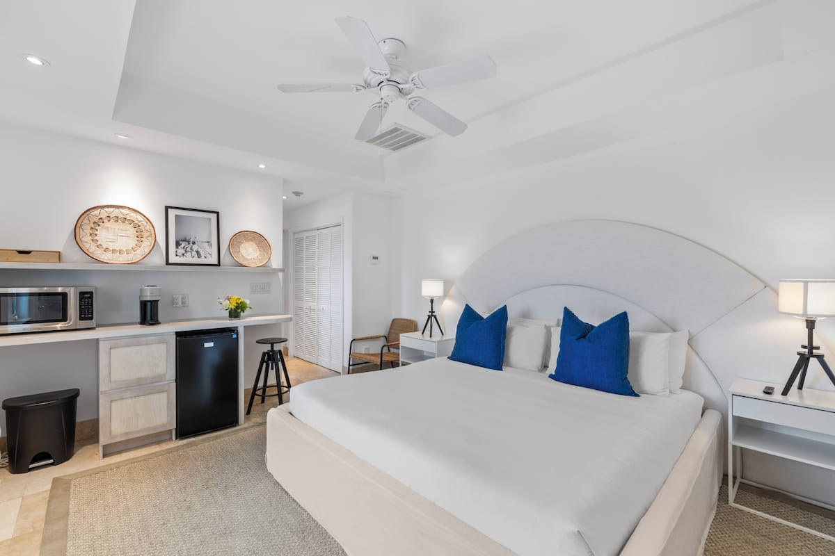 Une chambre d’hôtel moderne équipée d’un lit, d’un bureau, d’une kitchenette et d’un ventilateur de plafond.