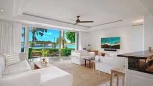 Amplia sala de estar con un gran ventanal con vistas a un paisaje marino, ventilador de techo y zona de cocina moderna.