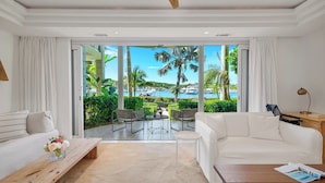 Habitación de hotel moderna con un sofá blanco, una mesa de centro de madera y vistas a una piscina y palmeras.