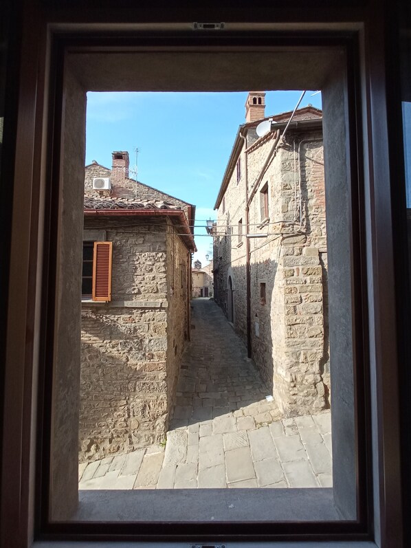 Une rue étroite bordée d’immeubles en pierre, avec une cheminée bien visible et un ciel bleu dégagé.