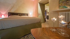 Een slaapkamer met een bed, nachtlampjes, een houten tafel met kaarsen en een schilderij aan de muur.