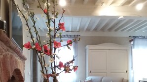 Een woonkamer met een open haard, een bank, een tapijtend met een rood patroon, en een vaas met bloemen.
