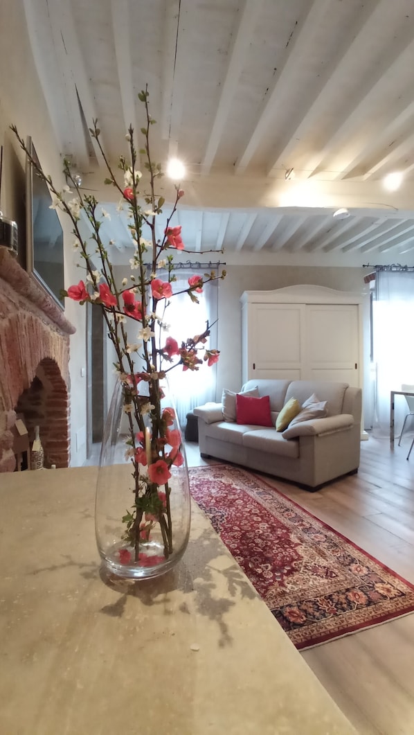 Ein Wohnzimmer mit Kamin, einer Couch, einem roten Teppich mit Muster und einer Vase mit Blumen.