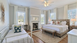 A spacious bedroom with a large bed, a bench, a fireplace, and a ceiling fan.