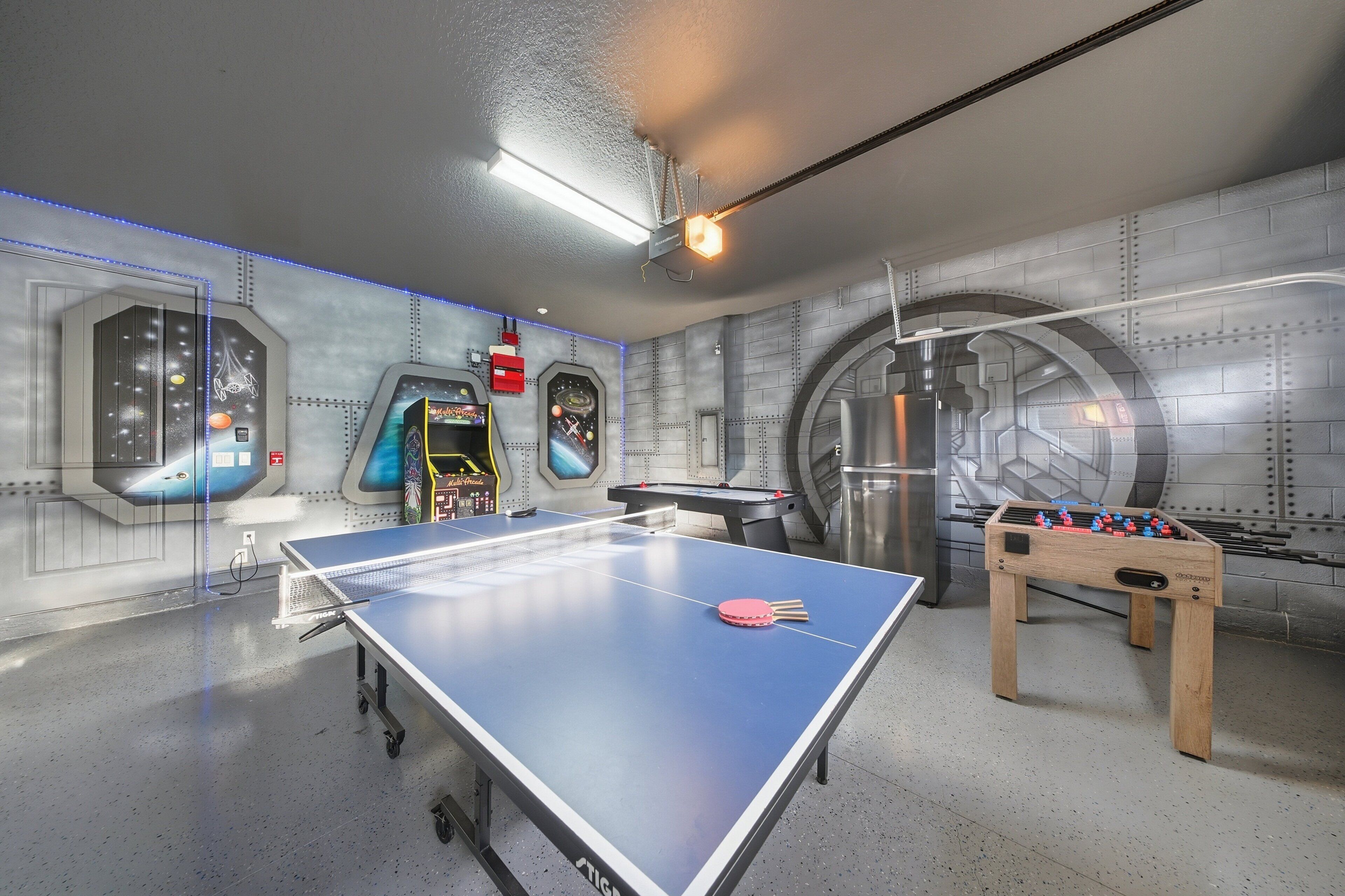Una habitación con mesa de fútbol de mesa, mesa de ping pong y máquinas de videojuegos.