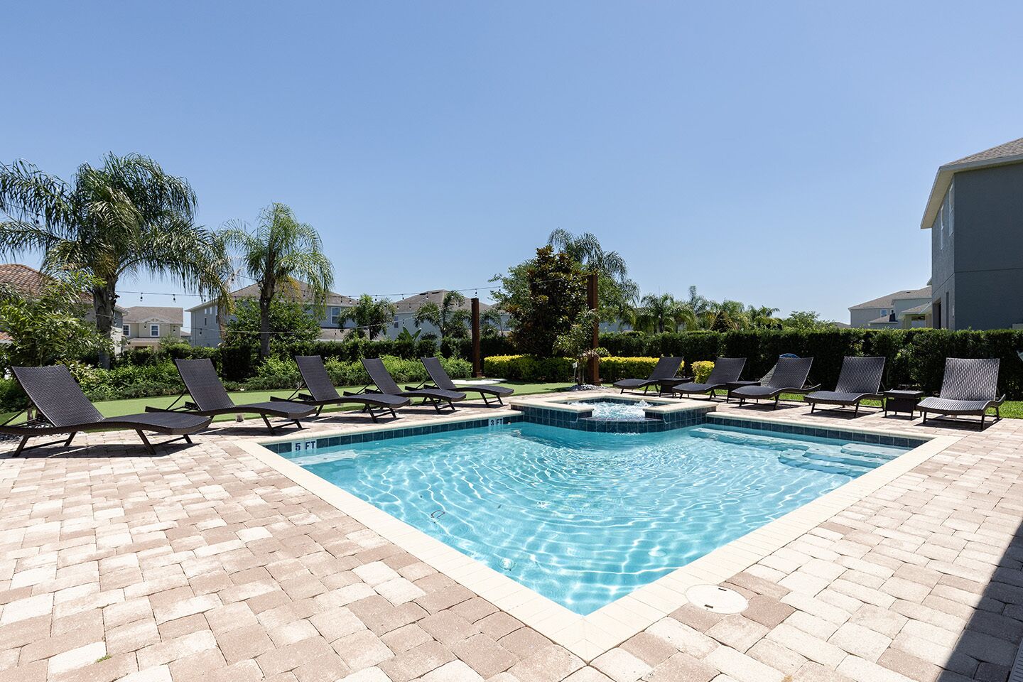 A rectangular swimming pool with a hot tub in the center, surrounded by lounge chairs and a brick patio.