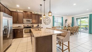 A modern kitchen with dark wood cabinets, stainless steel appliances, and a granite countertop island. - Charming Estate with Themed Bedrooms at Encore (Kissimmee)