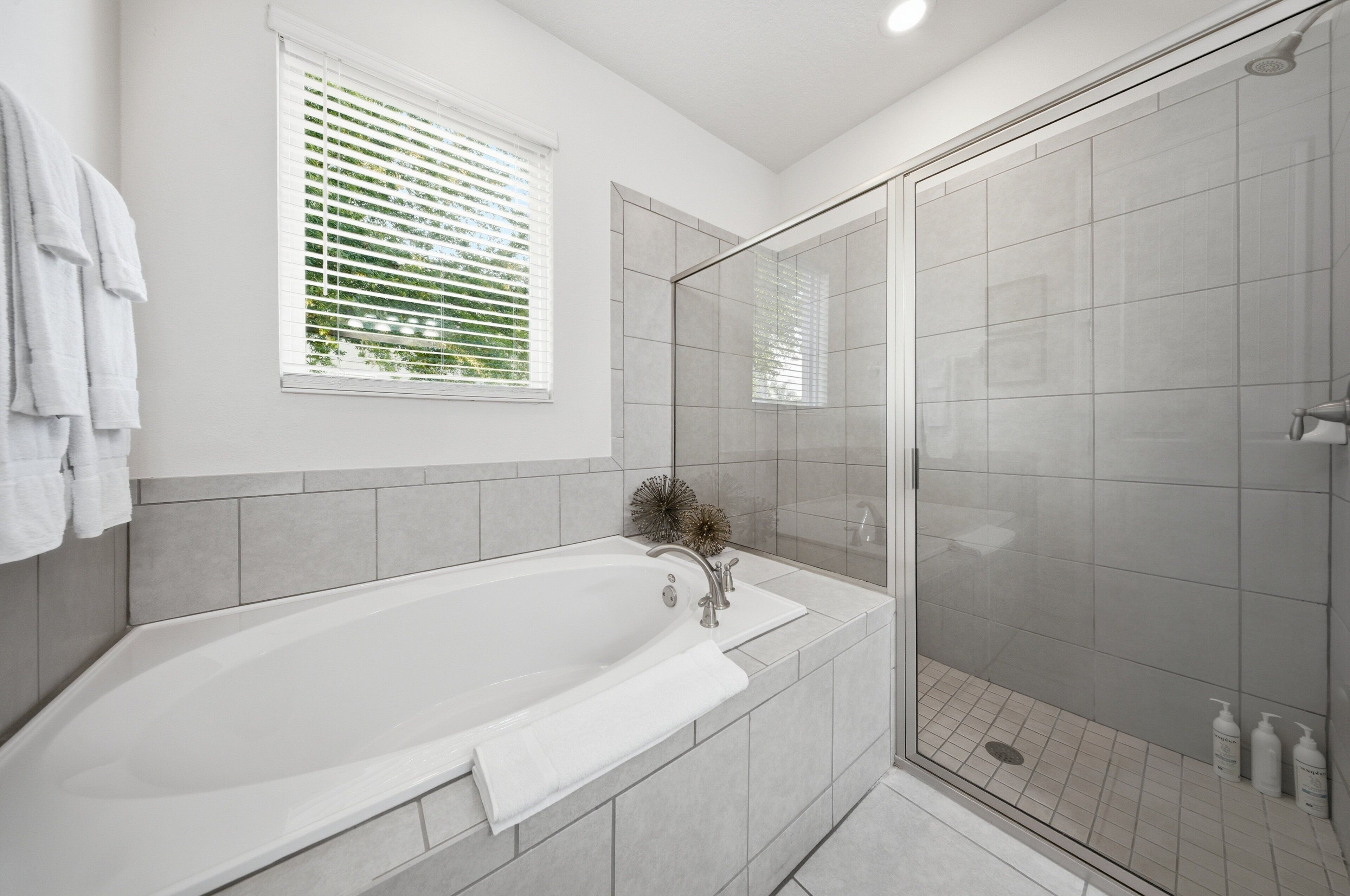 A modern bathroom with a bathtub, a glass-enclosed shower, and a window with blinds.