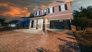 A two-story house with a garage, a driveway, and a landscaped front yard. - Charming Estate with Themed Bedrooms at Encore (Kissimmee)