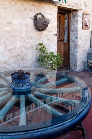 A rustic stone building with a wooden door and a glass table with a metal base.