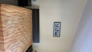 Een slaapkamer met een bed, nachtkastje, een wandplank en een ingelijste foto.