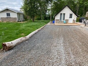 A gravel driveway leading to a small house with a stone foundation and a white exterior.