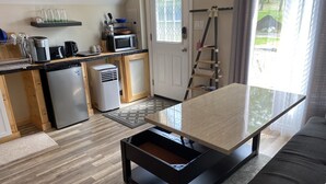 Eine kompakte Küche mit integriertem Geschirrspüler, einer Mikrowelle und einer Kaffeemaschine. Es gibt eine kleine Sitzecke mit einem Tisch und einer Couch.