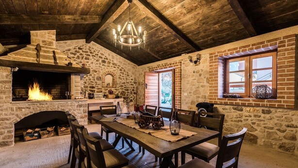 Un intérieur rustique en pierre avec une cheminée, une table à manger en bois et des chaises.