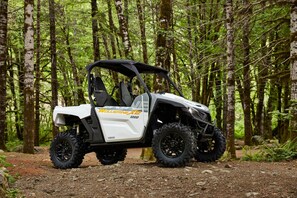 Valkoinen maastoauto, jonka kyljessä on teksti ”Wolverine X2 1000”, on pysäköity metsään.