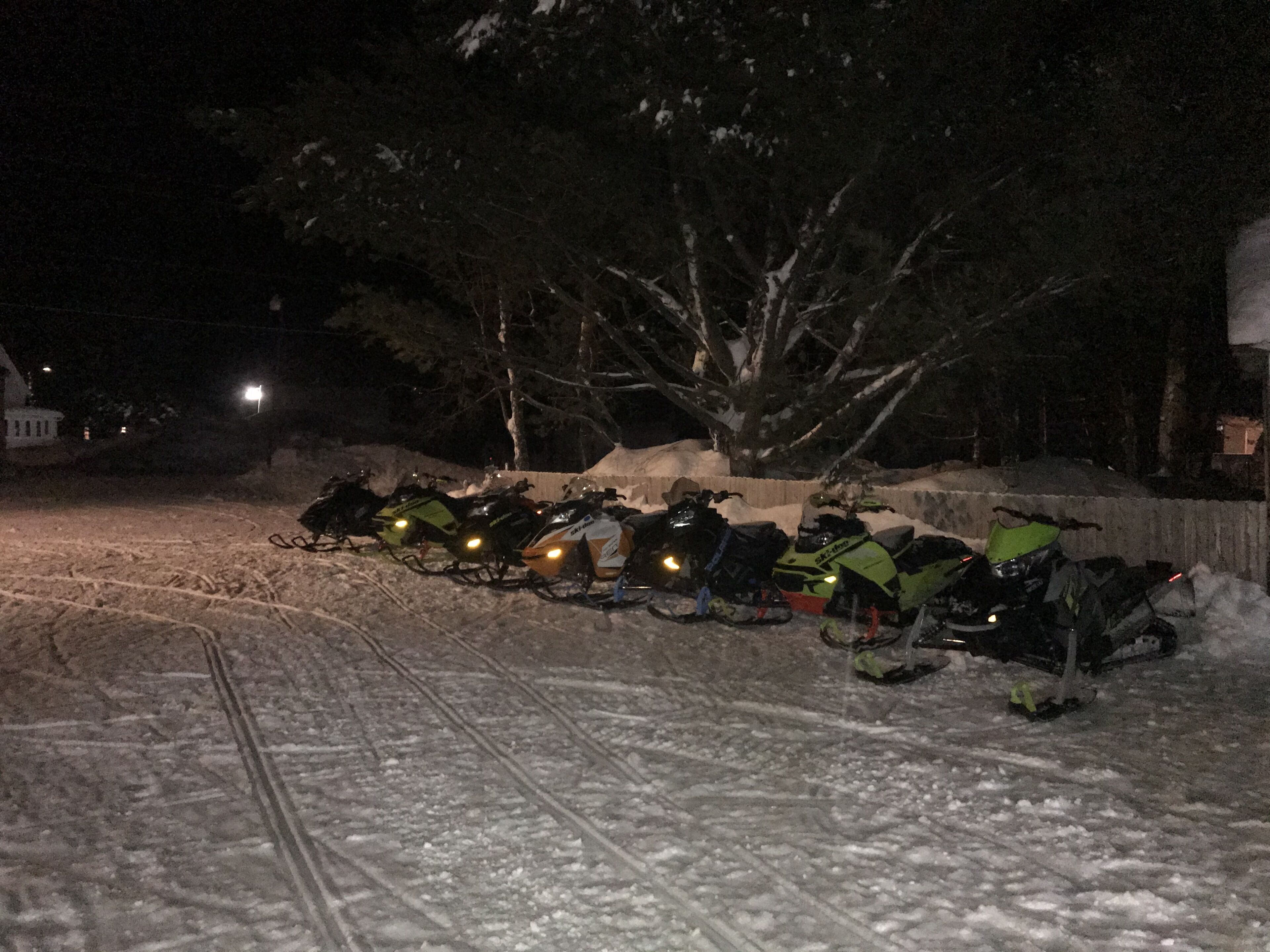 A row of snowmobiles parked on a snow-covered road at night.