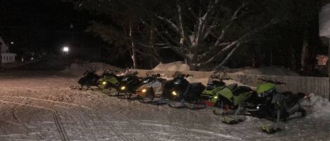 A row of snowmobiles parked on a snow-covered road at night.