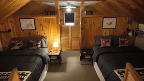 A cozy attic bedroom with two beds, a ceiling fan, and wooden walls.