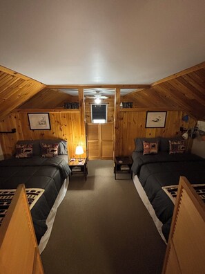 A cozy attic bedroom with two beds, a ceiling fan, and wooden walls.