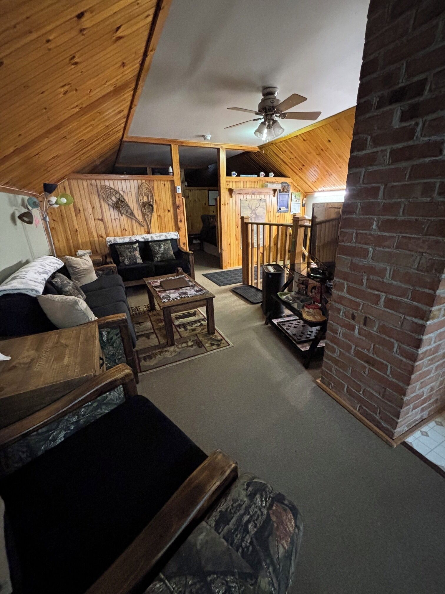 A cozy attic room with a sloped ceiling, wooden walls, a ceiling fan, a fireplace, and a seating area with a couch and coffee table.