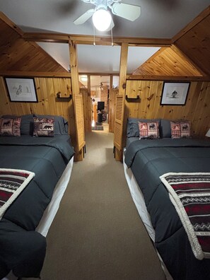 A room with two beds, wooden walls, a ceiling fan, and framed pictures on the walls. - Majestic Recreational Lodging w/ Snowmobile and Side x Side rentals on Long Lake (Sinclair)