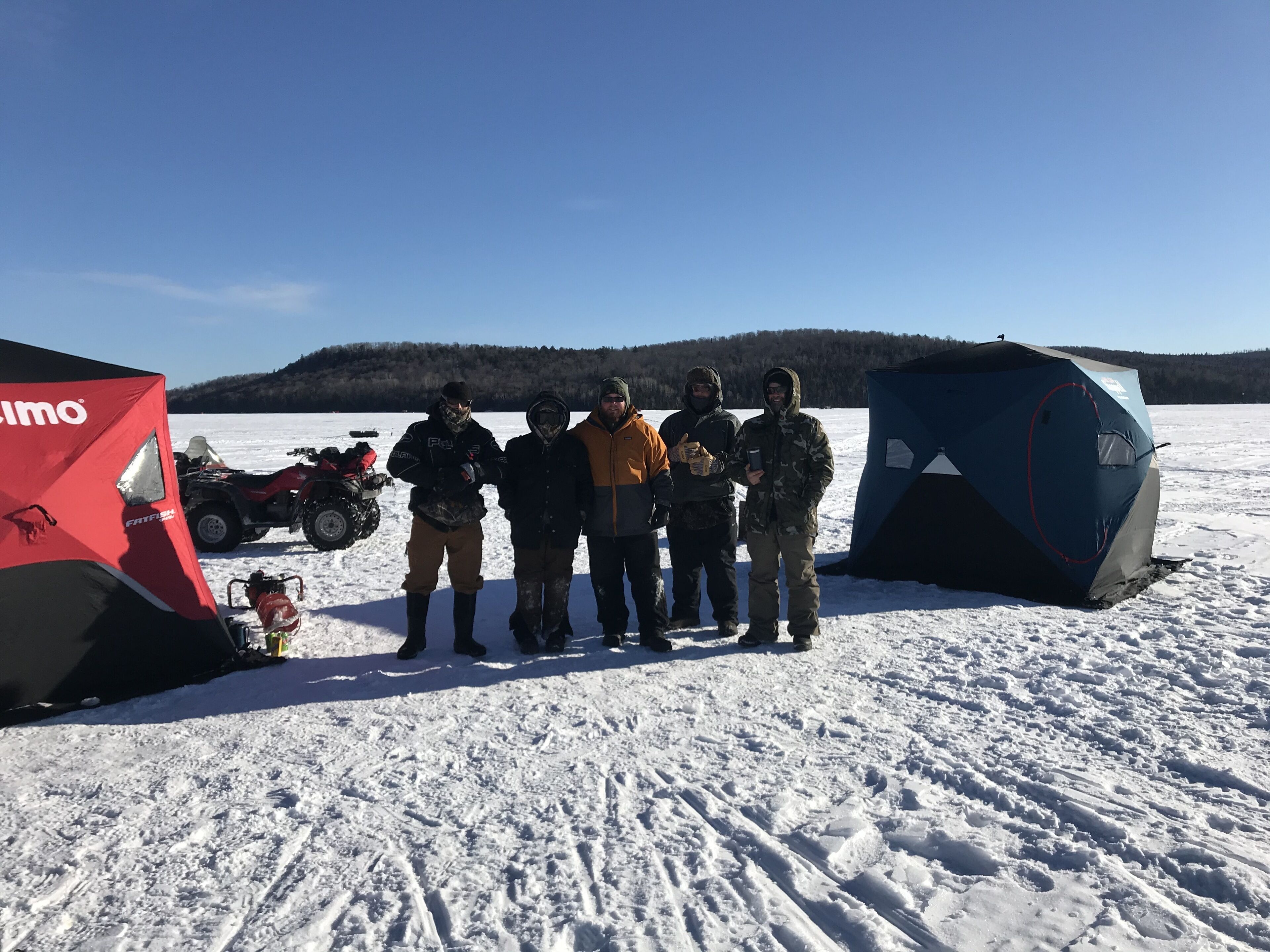 A group of people standing in a snowy outdoor area with tents and an ATV.