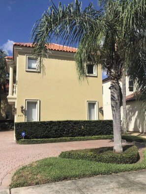 A two-story building with a flat roof, a small window on each floor, and a well-maintained hedge in front.